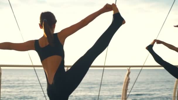 Yoga classe mulher grupo prática ioga Hand-to-Big-Toe Pose pôr-do-sol mar câmera lenta — Vídeo de Stock