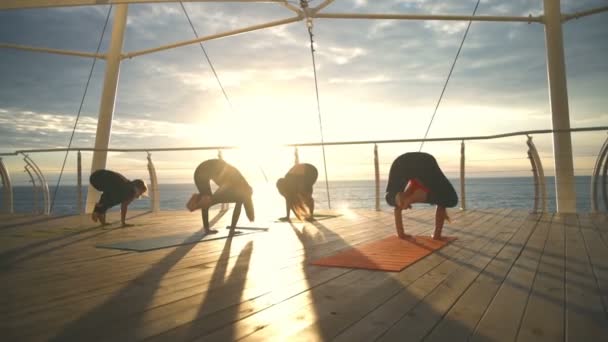 Yoga classe grupo menina prática ioga guindaste Pose pôr do sol mar câmera lenta — Vídeo de Stock