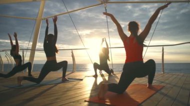 Yoga sınıfı grup genç kızı pratik yoga Anjaneyasana gün batımı deniz ağır çekim