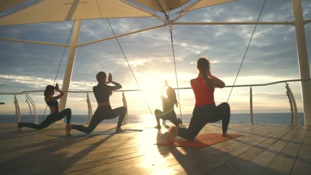 Yoga klasse groep jonge meisje praktijk yoga Anjaneyasana zonsondergang zee Slowmotion — Stockvideo