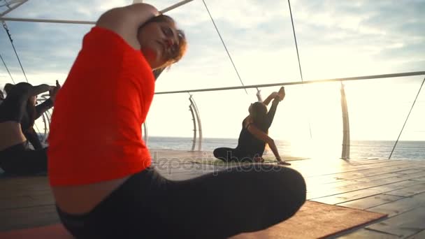 Clase de yoga grupo de mujeres jóvenes practican yoga brújula pose amanecer océano cámara lenta — Vídeos de Stock