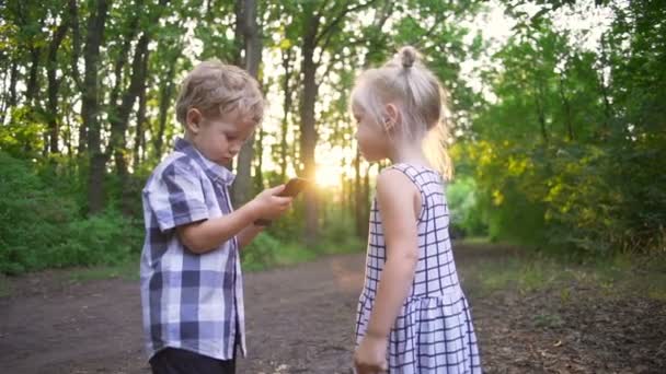 Vackra barn pojke och flicka använda smartphone solig park snabba slowmotion — Stockvideo