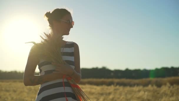 Jong meisje in veld met boeket tarwe rood lint Flutter zon snelle slow-motion — Stockvideo