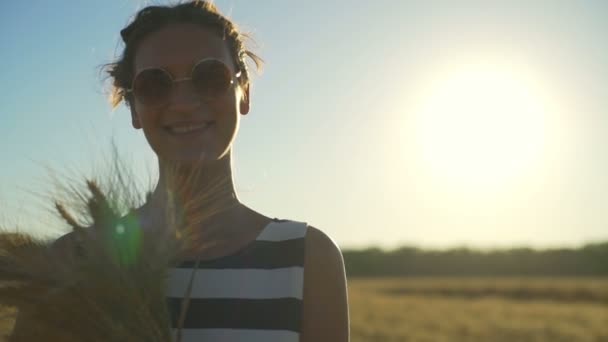 Schöne Mädchen lächelnd Sonnenbrille bleiben Feld Strauß Weizen Sonne schnelle Zeitlupe — Stockvideo