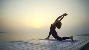 Genç kız ince siyah giymek yapmak yoga düşük hamle poz gündoğumu sis hızlı yavaş hareket