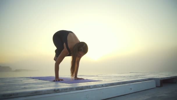 Flexible Frau schlank schwarz tragen Yoga Kranich posieren Sonnenaufgang Nebel schnelle Zeitlupe — Stockvideo
