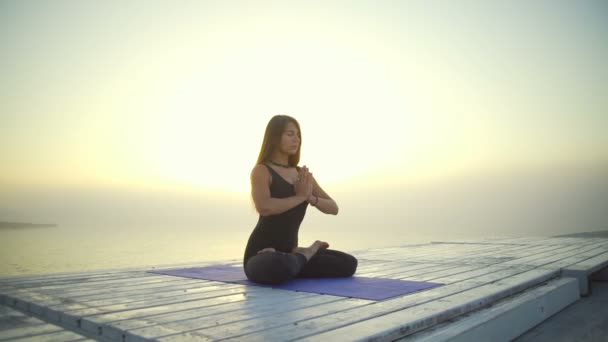 Junges Mädchen schlank schwarz tragen Yoga Lotus Namaste Pose Sonnenaufgang Nebel schnelle Zeitlupe — Stockvideo