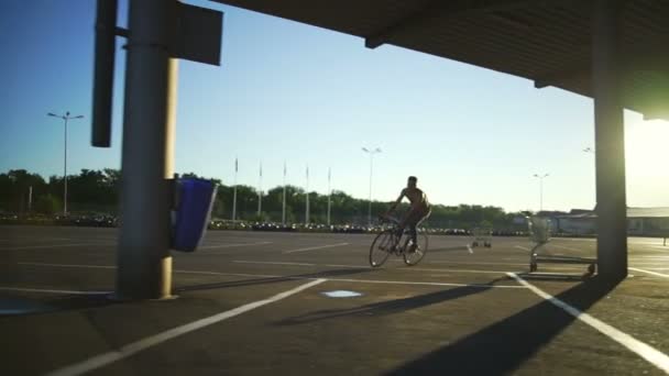 Niño montando una bicicleta en el aparcamiento vacío centro comercial salida del sol cámara lenta rápida — Vídeo de stock