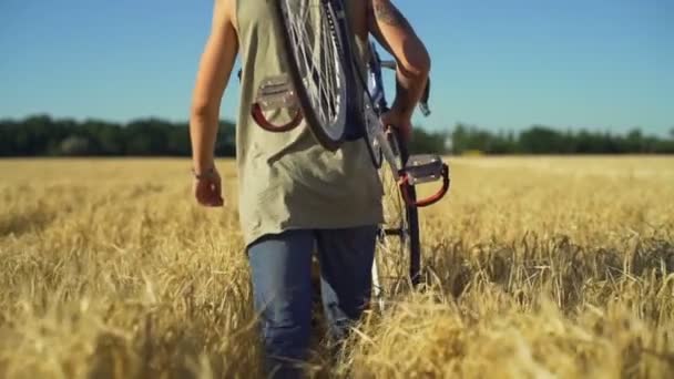 Крупный план человек нести велосипед ходить по пшеничному полю заката замедленного движения быстро — стоковое видео