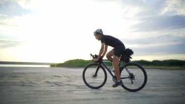 Yakışıklı bisikletçi binmek bisiklet kask kum Sahil gün batımından yavaş hareket hızlı