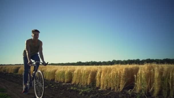 Vacker ung pojke ridning cykel nära vete fält sundown slowmotion snabb — Stockvideo