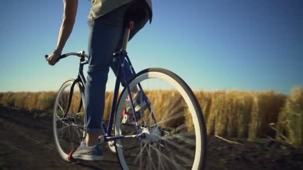 Fuerte joven montar en bicicleta cerca de campo de trigo puesta del sol cámara lenta rápida — Vídeo de stock