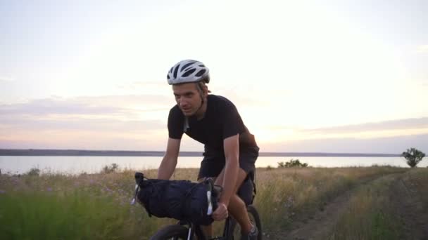 Jovem ciclista preto terno capacete passeio de bicicleta vale estrada amanhecer câmera lenta rápido — Vídeo de Stock