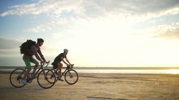 Молодые велосипедисты ездят вместе шлемы песок на берегу моря рассвет замедленное движение быстро — стоковое видео