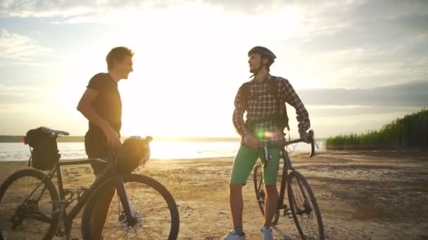 Dos ciclistas sonrientes se encuentran estrechan la mano al mar amanecer cámara lenta rápido — Vídeo de stock