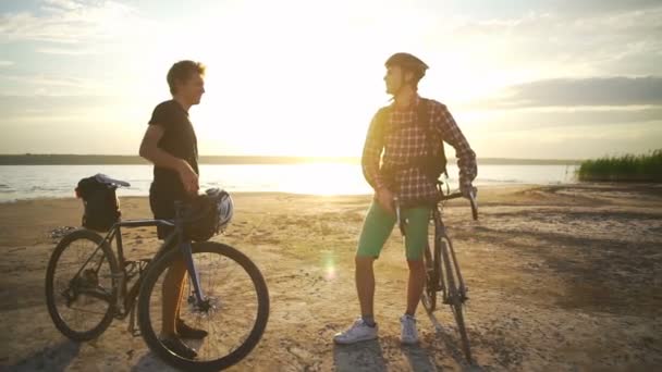 Doi tineri cicliști se întâlnesc reciproc scutură mâinile pe litoral în zori lent mișcare rapidă — Videoclip de stoc