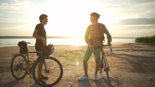 Twee jonge fietsers ontmoeten elkaar schudden handen aan zee dawn slowmotion snelle — Stockvideo