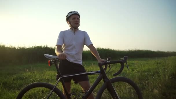 Ciclista deportivo estancia con bicicleta verde hierba casco soleado rápida cámara lenta — Vídeos de Stock