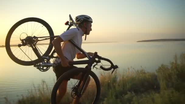 Fuerte ciclista lleva bicicleta en el hombro correr por la costa vista al mar rápida cámara lenta — Vídeo de stock