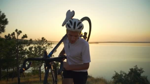 Ciclista forte carrega bicicleta no ombro penhasco mar pôr do sol movimento lento rápido — Vídeo de Stock