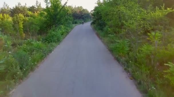 Fietser rijden fiets asfalt weg zonnige bos helm zonsondergang drone beelden — Stockvideo