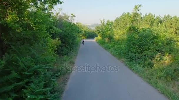Bicicleta paseo bicicleta asfalto carretera en soleado bosque casco puesta del sol drone metraje — Vídeos de Stock