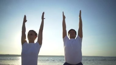 Bir grup insan yoga poz namaste sahil gündoğumu hızlı yavaş hareket yapıyor