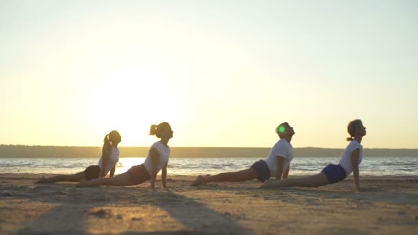 Mensen doen yoga plank omhoog neerwaartse gezicht hond vormt zee dawn snelle slow-motion — Stockvideo