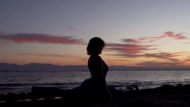 夕暮れ時に海の海岸で双子の上に座ってストレッチを行う女性のシルエット — ストック動画