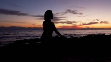 Siluet kadın renkli günbatımında denize karşı meditasyon yapıyor.