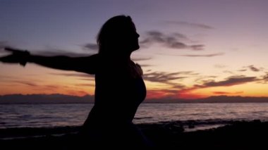 Kızın silueti namaste pozisyonunda oturur gün batımında deniz kenarında meditasyon yapar.