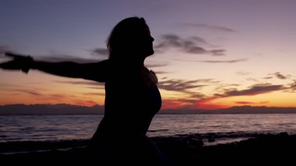 Silhouette di ragazza si siede in posa namaste meditando sul mare al tramonto — Video Stock