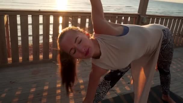 Menina branca flexível que se estende na postura do ioga do triângulo no telhado no brilho do sol — Vídeo de Stock