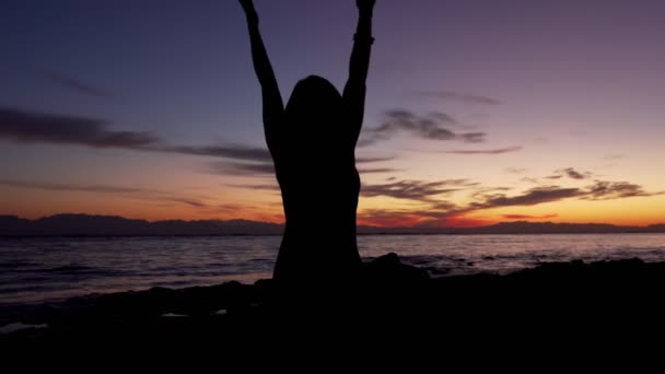 석양이 떠 있는 바닷가 포즈로 로터스 에서 명상을 하고 있는 소녀 실루엣 — 비디오