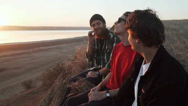 Kaykaycılar gün batımında deniz kıyısında ot tüttürüyorlar.