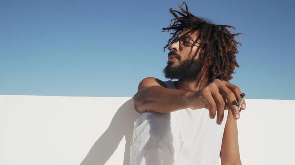 Arka planda mavi gökyüzü olan, çatıda ot içen siyah bir adam.