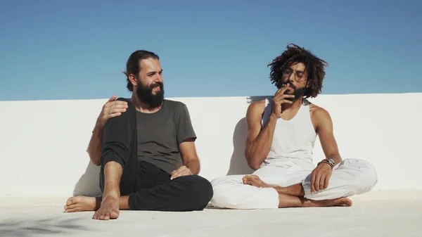 Çok kültürlü arkadaşlar arka plandaki mavi gökyüzünde ot içip eğleniyorlar.