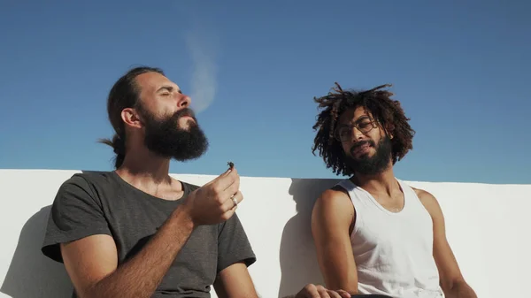 Мультикультурные друзья веселятся и курят травку на фоне голубого неба на крыше — стоковое фото