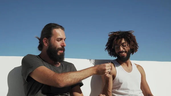 Çok ırklı arkadaşlar çatıdaki mavi gökyüzünde ot içiyorlar.