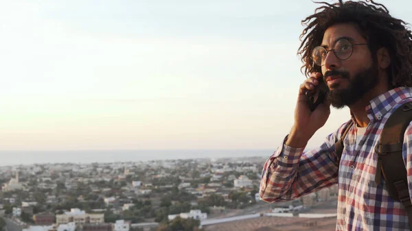 Çekici gezgin erkek gün doğumunda bir uçurumun kenarında telefonla konuşuyor.