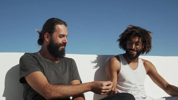 Çok ırklı arkadaşlar çatıdaki mavi gökyüzünde ot içiyorlar.