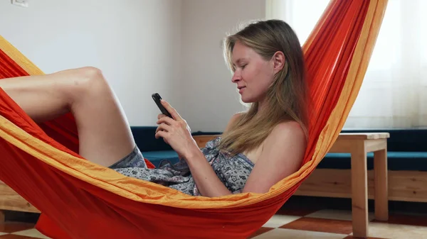 Hamakta cep telefonuyla gülen mutlu sarışın kız.