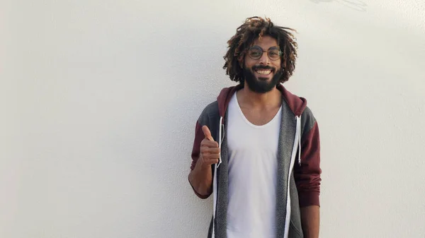 Preto homem sorriso e mostrar sinal polegares para cima no branco parede no fundo — Fotografia de Stock