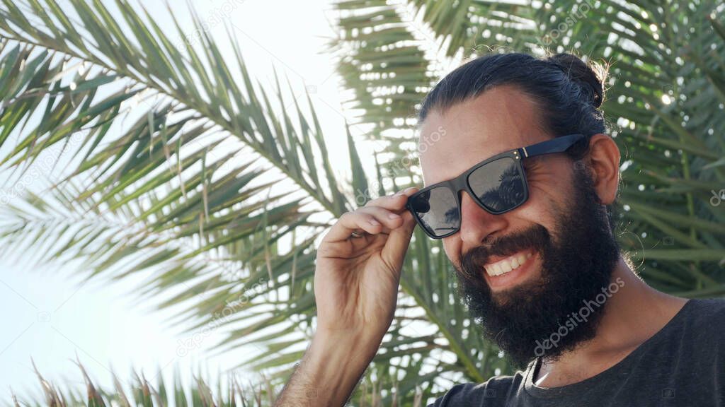 Man putting off sunglasses and look in camera on a background of palm leaves