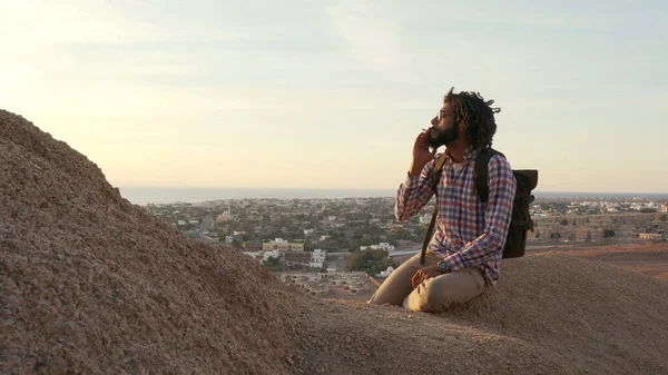 Взрослый африканский мужчина курит косяк с марихуаной, сидящей на утесе на рассвете — стоковое фото