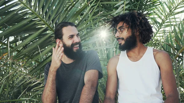 Два парня разных национальностей разговаривают на фоне пальмовых листьев — стоковое фото