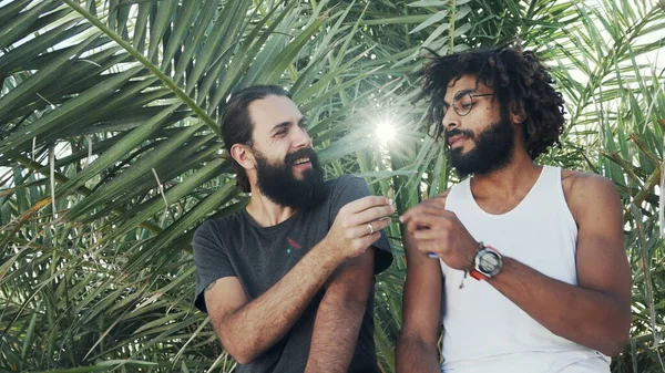 Os amigos multiétnicos dão um a outro uma união com a erva daninha em um contexto de folhas de palma — Fotografia de Stock