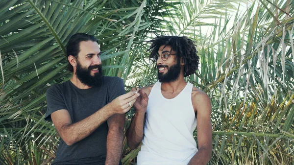 Os amigos multiétnicos dão um a outro uma união com a erva daninha em um contexto de folhas de palma — Fotografia de Stock