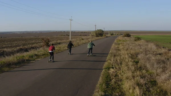 Gün batımında çayırda kaykay yapan üç yeniyetme adamın hava görüntüsü.