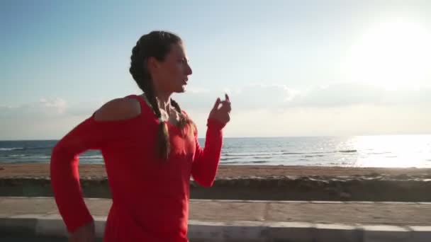 Athletic woman jogging on the promenade by the ocean at sunrise slow motion — Stockvideo